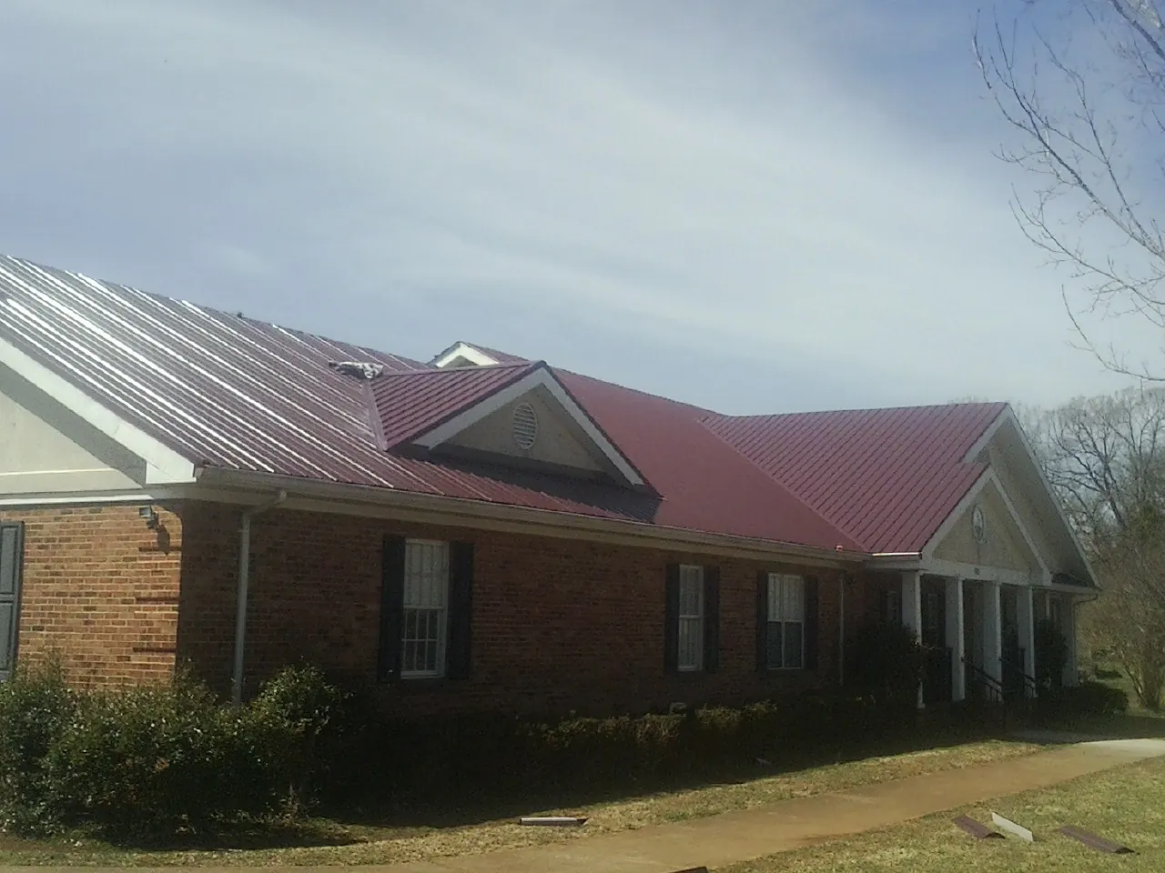 Red metal roof with gabled entries on a long brick building, from a Hail Damage Roof Repair job in Waterloo