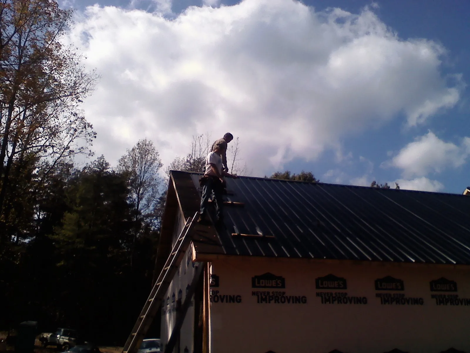 Roofer fastening dark metal panels high against a cloudy sky, from a Roof Inspection job in Waterloo